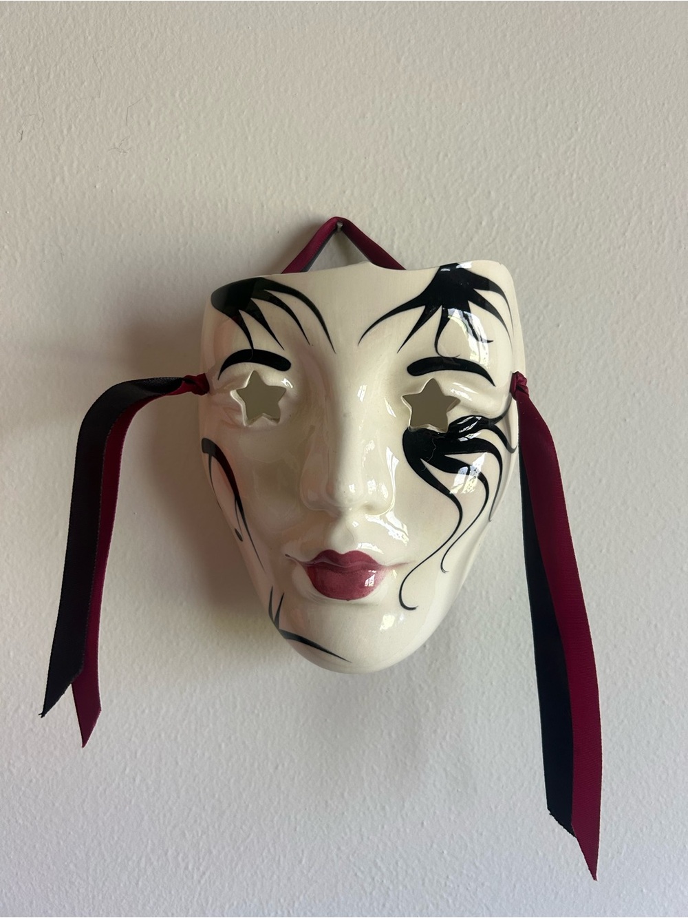 Decorative White Ceramic Mask Wall Art with Black Accents and Burgundy Ribbon